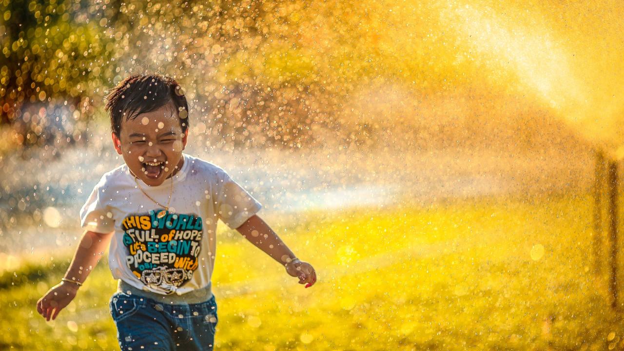 boy running through sprinkler 